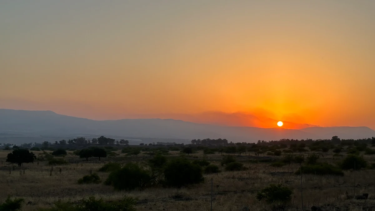 Sun setting behind layered mountain ridges above an open valley